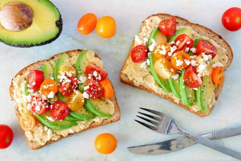 Two pieces of toast with hummus, avocados, and tomatoes