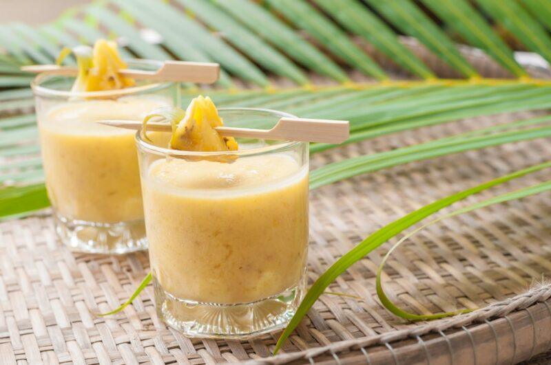 Two glasses of pineapple big youth cocktail, with leaves in the background