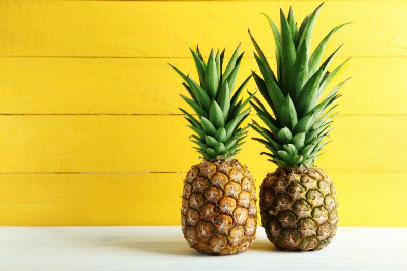 Two fresh pineapples against a yellow background