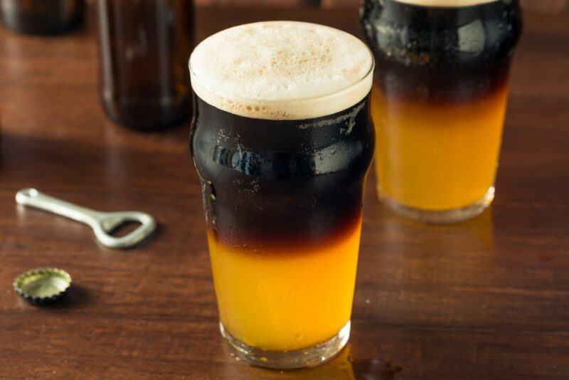 A few pint glasses containing a black and tan cocktail on a wooden table