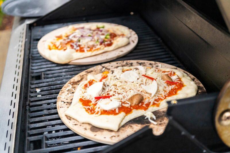 A large grill with two homemade pizzas on pizza stones that are ready to be eaten