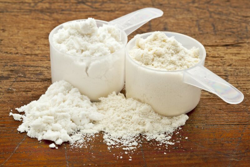 Two plastic scoops containing whey protein powder against a wooden background