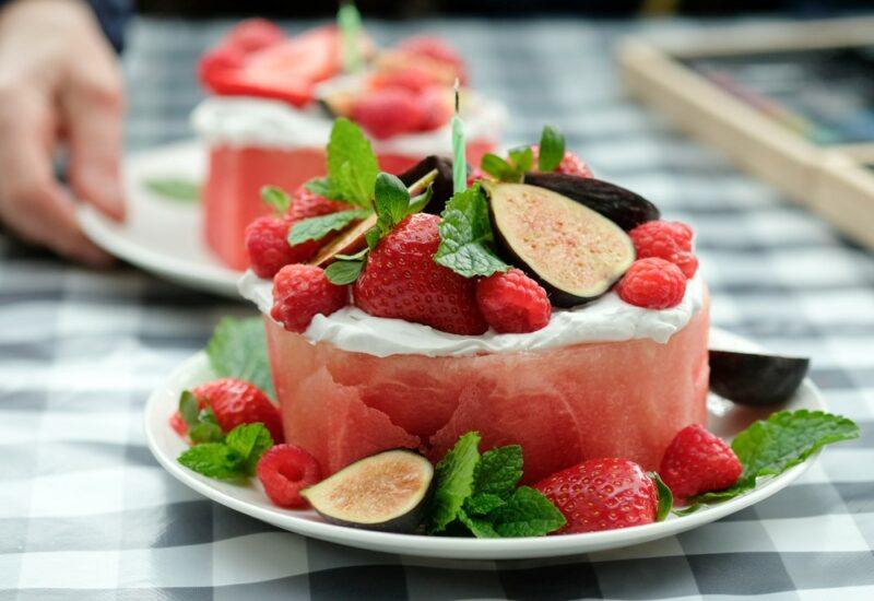 Two plates with a cake that is made from watermelon and topped with figs and berries