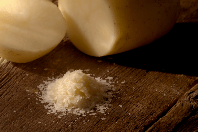 A dark wooden table with two potatoes and a small pile of potato flakes.