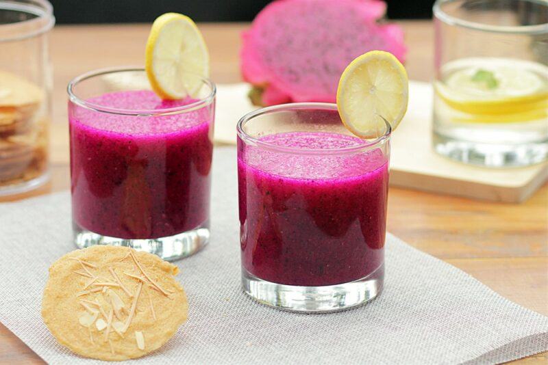 Two glasses of dragonfruit fruit juice with more glasses and some dragonfruit in the background