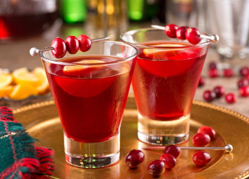 Two cranberry cocktails in short glasses, each garnished with cranberries on a cocktail pick