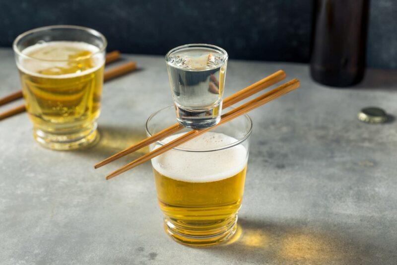 A glass of beer with a sake shot balanced on top of it, with a second glass of beer in the background