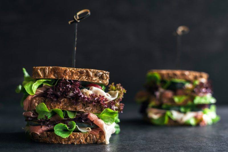 Two sandwiches on a table, made with whole grain bread and stuffed full of healthy ingredients