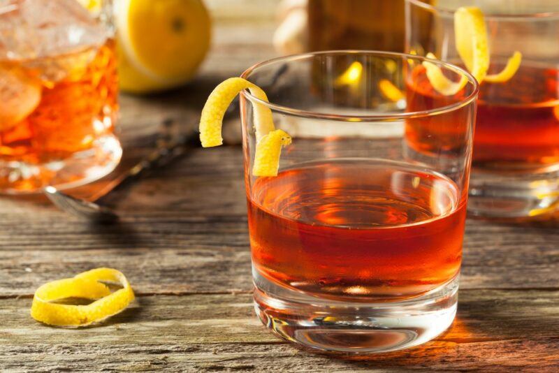 A wooden table with three sazerac cocktails, each with a lemon twist