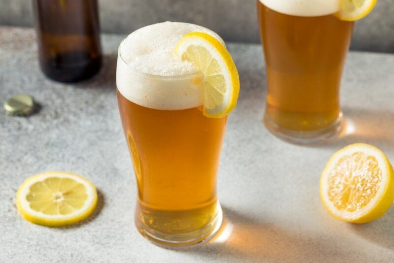 Two beer and soda shandies on a table, next to some lemon pieces