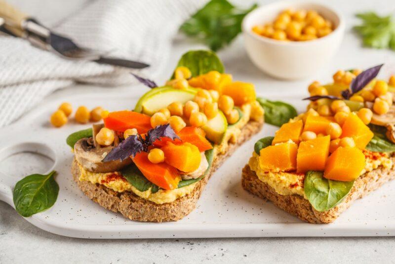 Two pieces of bread with hummus, chickpeas, squash, and other ingredients as toppings