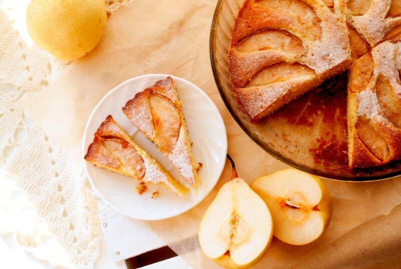 A pear tart in a dish on a table, next to a plate with two pieces of the tart