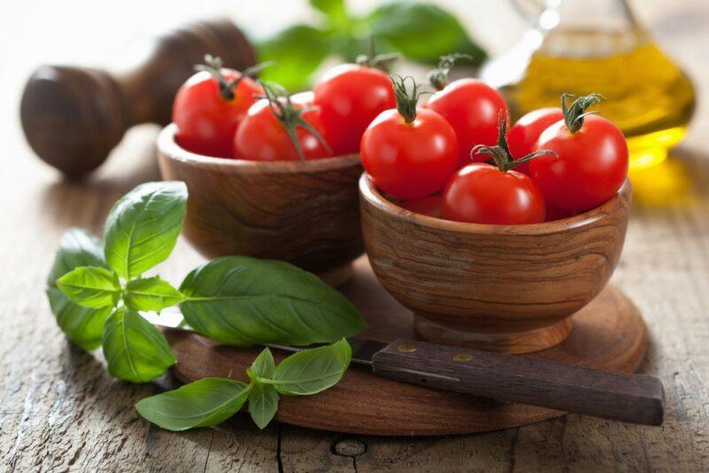 Two small wooden bowls containing cherry tomatoes next to basil