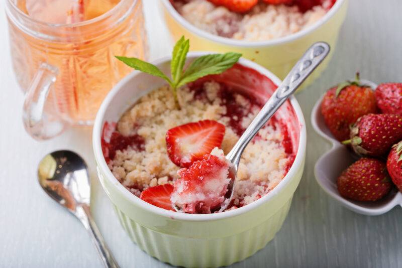 Two small dishes of a strawberry cobbler, next to a small bowl of strawberries and a mug of soda