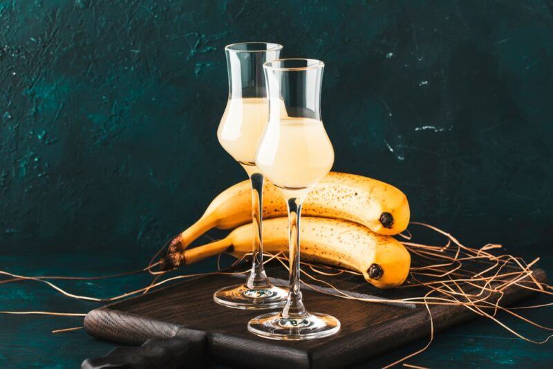 Two small glasses containing climax moonshine banana drops, in front of two bananas