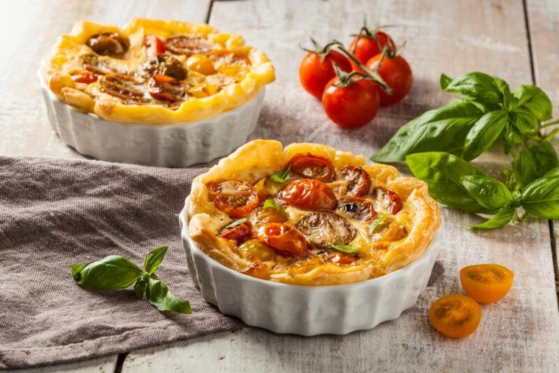 Two small quiches with cherry tomatoes in tart pans on a table