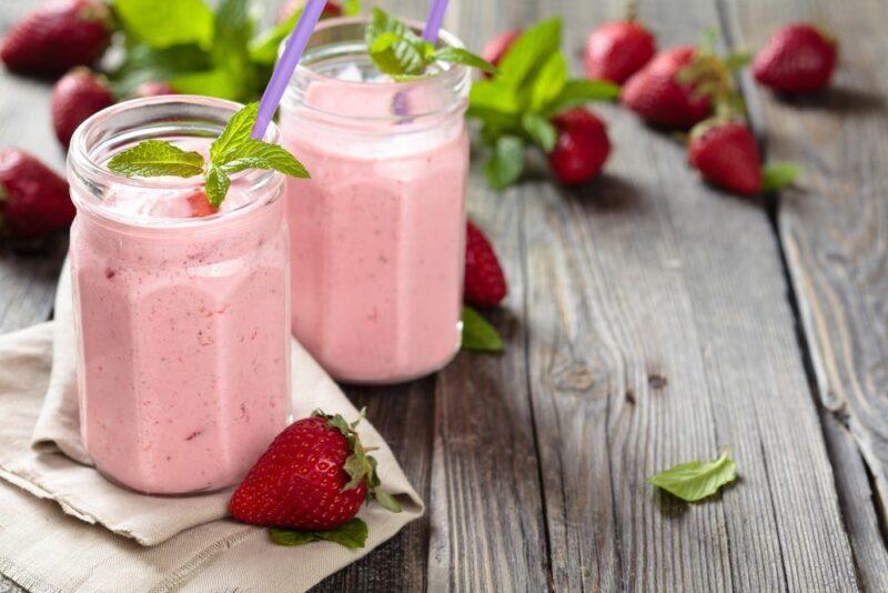 Two glasses of a strawberry smoothie on a wooden table with strawberries scattered around