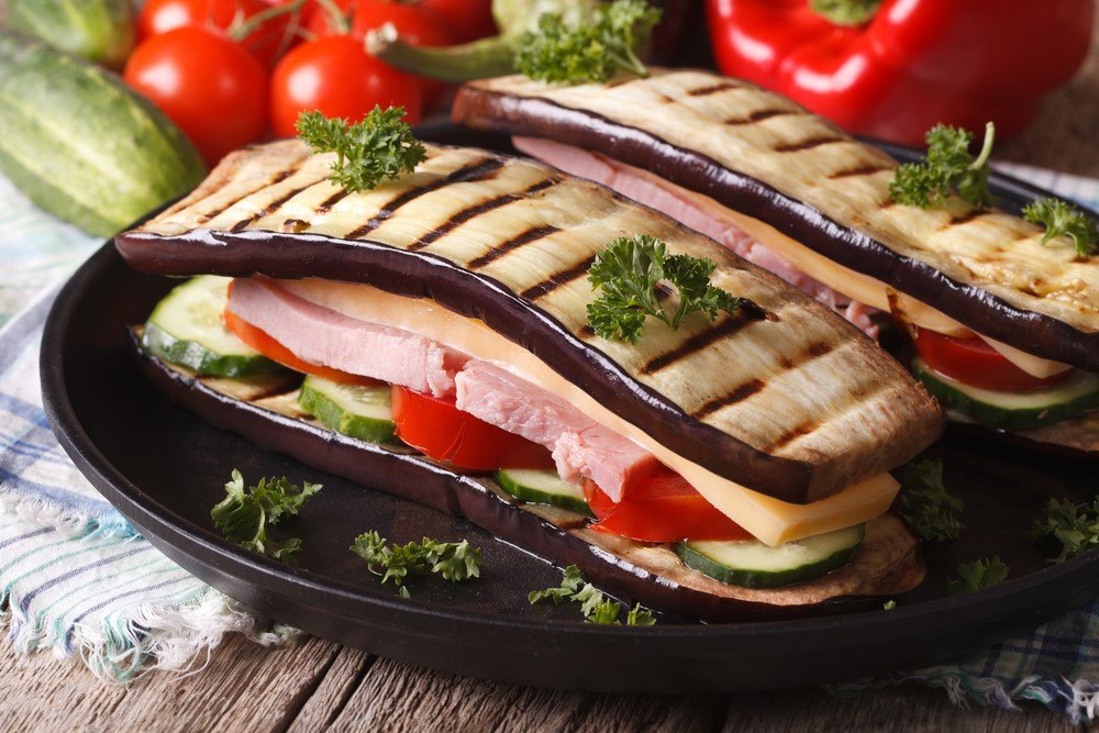 A black plate with two sandwiches that use eggplants instead of bread