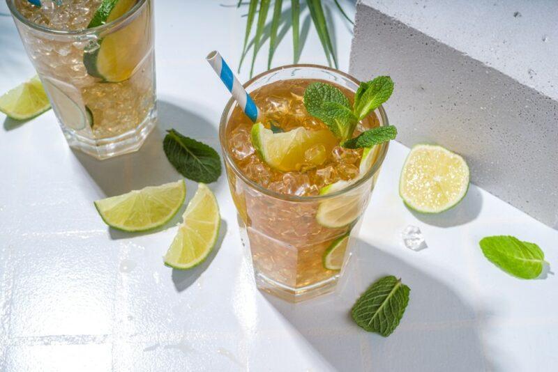 Two tall glasses of an ancient mariner cocktail with limes scattered on the table