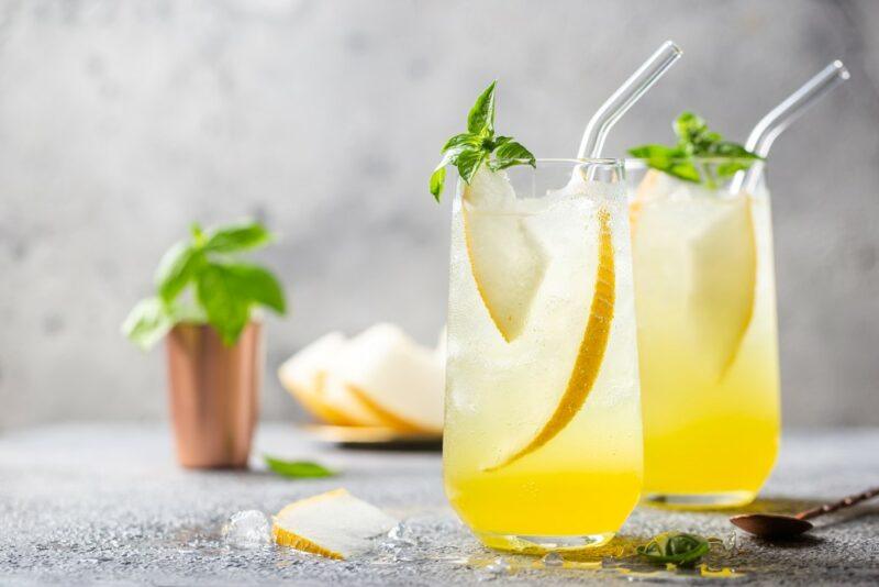 Two tall glasses containing a citrus rum cooler, with pieces of peer