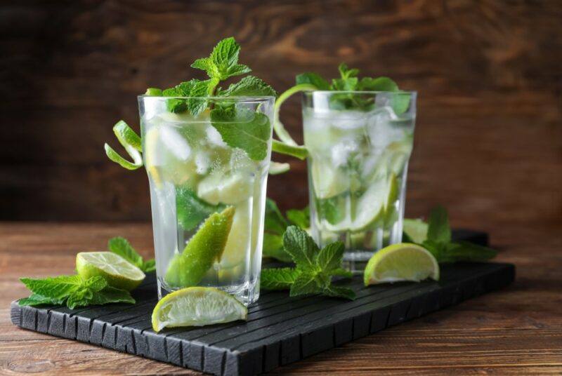 Two tall glasses containing mojitos, with plenty of ice, limes, and mint