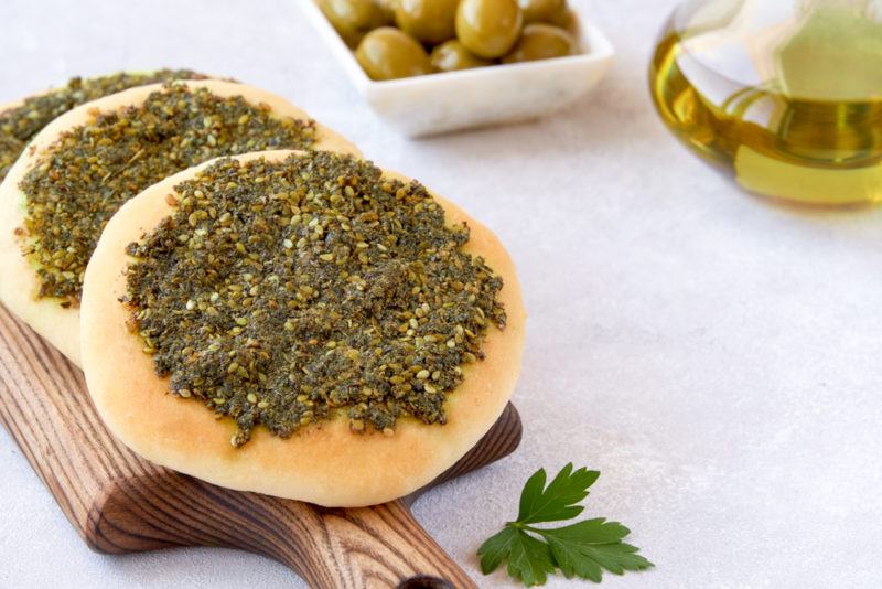 Two pieces of zaatar manouche on a wooden board near some olives and olive oil