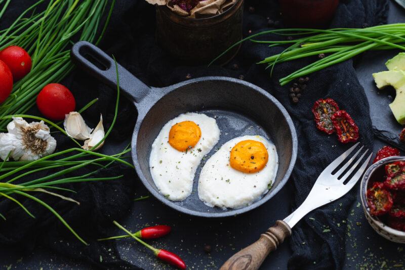 Two vegan eggs in a cast iron pan surrounded by herbs and other ingredients, highlighting the idea of plant-based egg brands