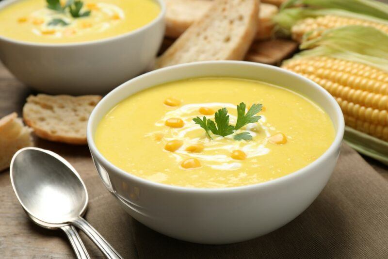 Two white bowls filled with corn soup, with spoons