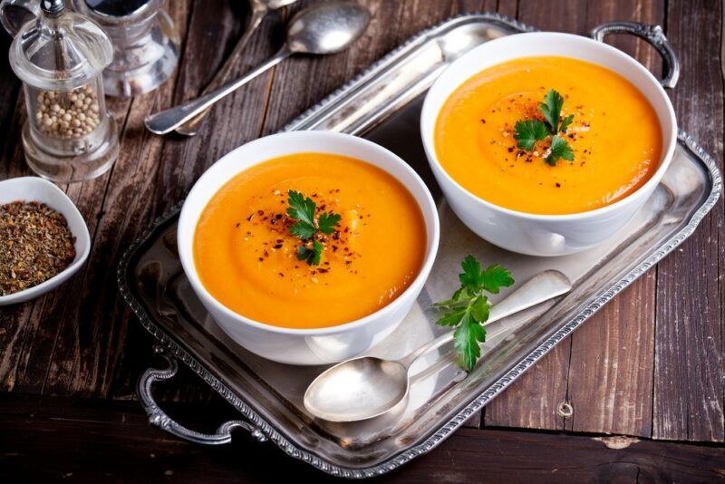 Two white bowls filled with pumpkin soup, with various spices in the background