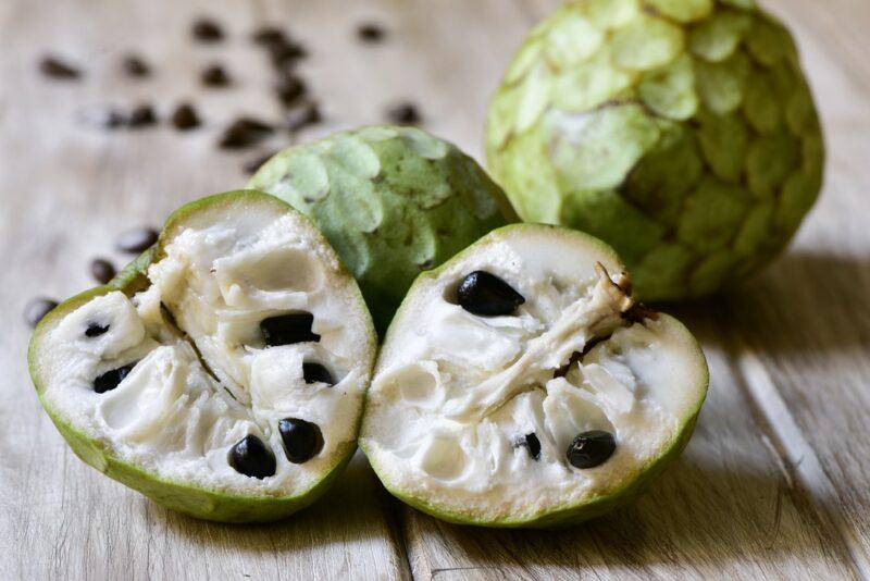 Two whole cherimoya fruit with two halves of the fruit and a handful of seeds