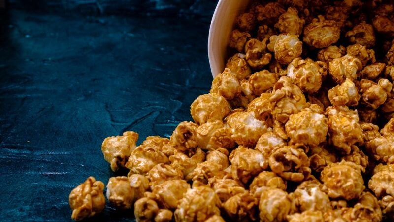 A large container of vanilla cardamom popcorn spilling onto a blue table