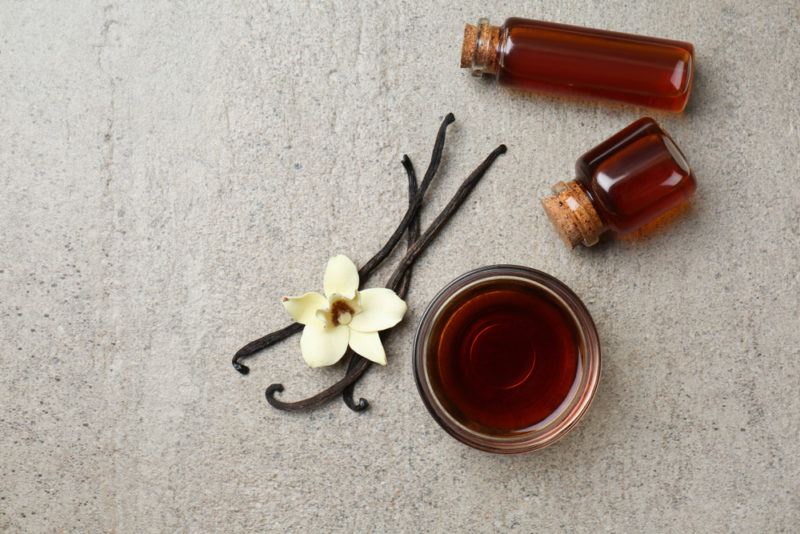 A bowl of vanilla extract, two bottles and vanilla beans