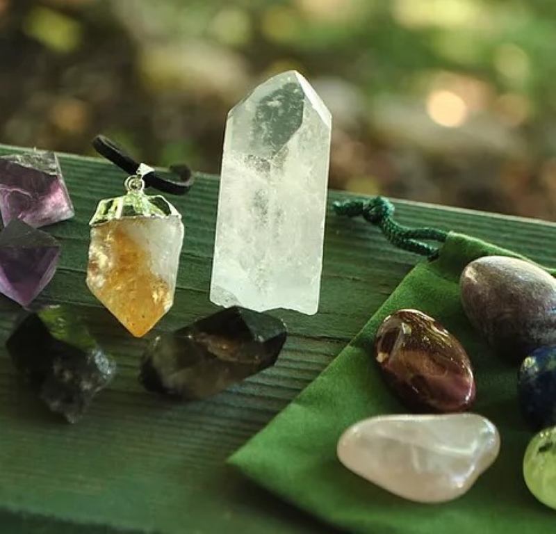 Several different stones on a green background on the left rough crystals one on a leather lanyard, on the right polished stones sitting on a green carrying bag