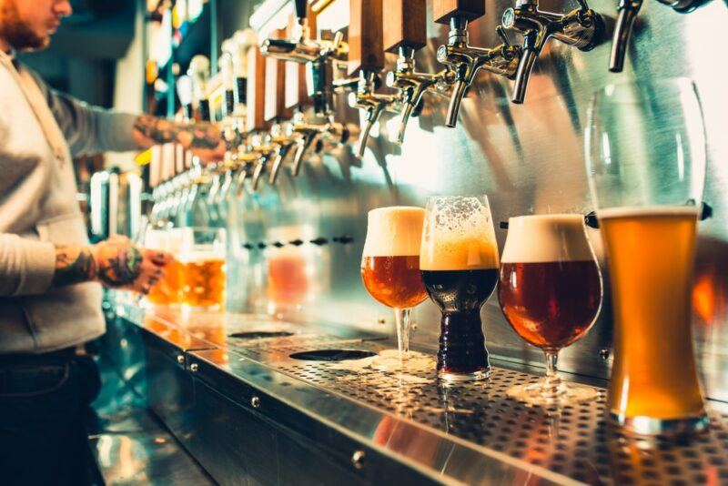 A bar, where a selection of beers are being poured from taps. There's a bartender on the far left