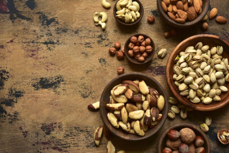 A selection of bowls of different sizes that contain various nuts, on a wooden background