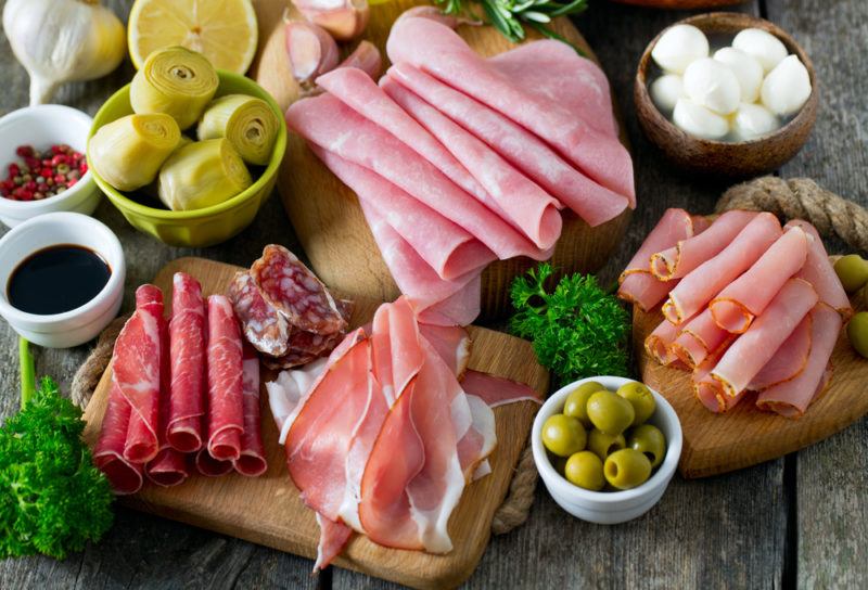 A selection of cold cut meats, olives, artichokes, cheese, and dips on boards