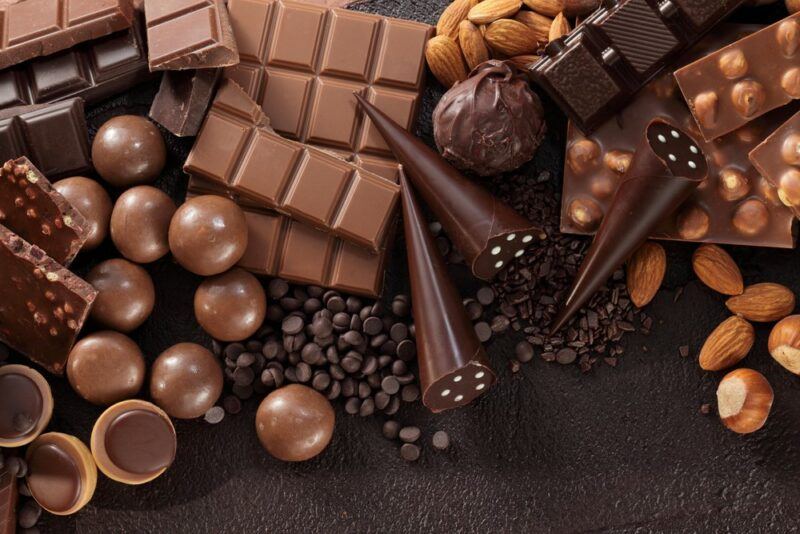 A dark table with various types of chocolate, including chocolate drops, cones, and balls. There are a few nuts on the table too.