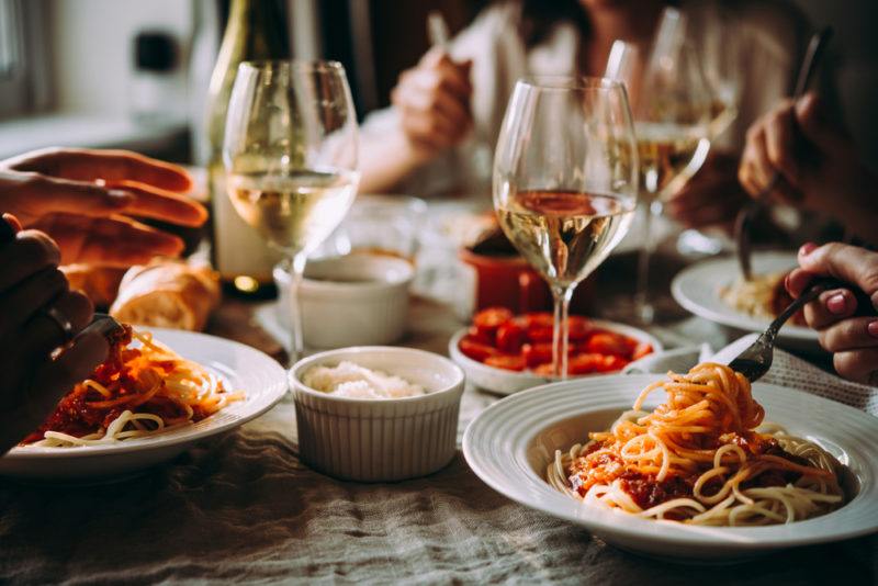 A table with white plates of pasta and glasses of wine