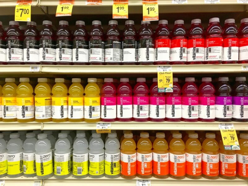 A grocery store shelf showing many different bottles of Vitaminwater with price tags