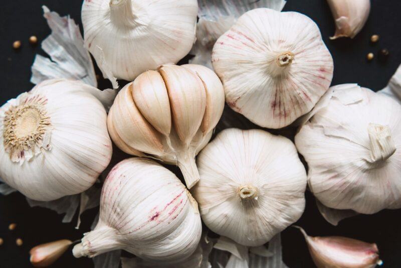 A selection of fresh garlic bulbs on the ground, one of which has had its skin removed