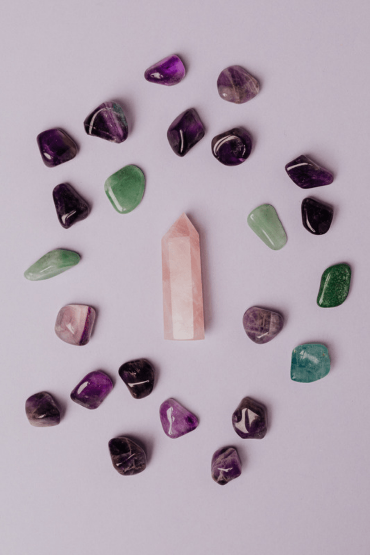 Various polished gems including amethyst, rose quartz, quartz, and jade on a light purple background