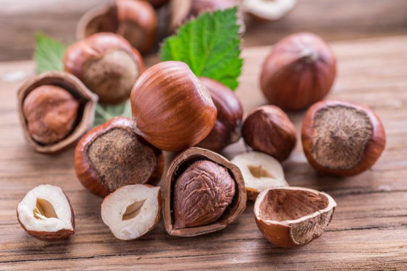 A selection of hazelnuts on a table. Some are whole, some have been opened or split and there are some leaves as well