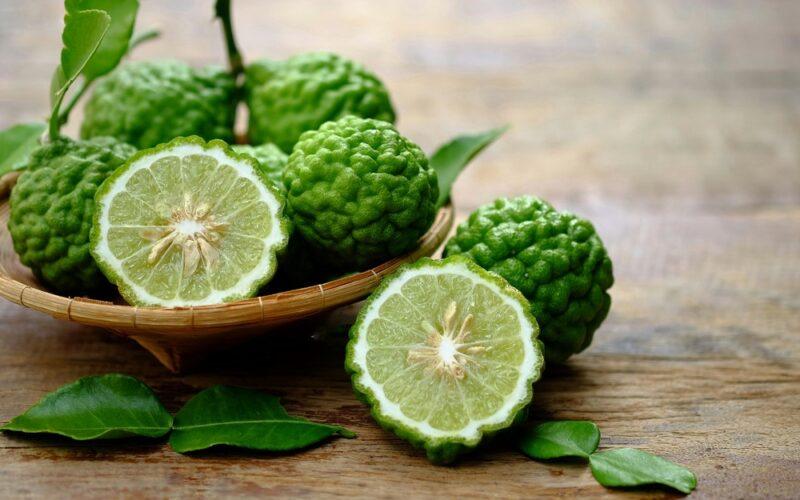 A wooden bowl containing kaffir limes with bumpy skin, plus one that's been cut in half