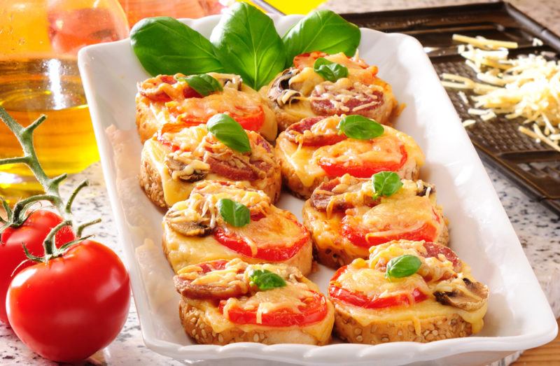 A white dish of mini pizzas made using bread as the base