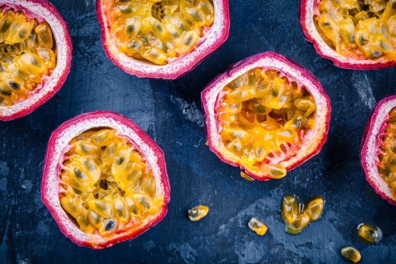 A flat lay image of a blue table with passion fruit that have been cut in half