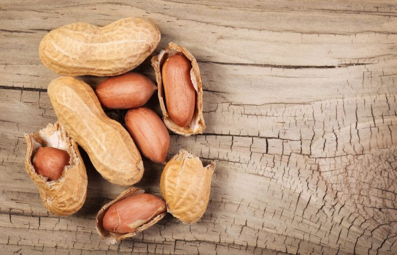 A wooden board with peanuts in their shells, some where the shell has been partly removed