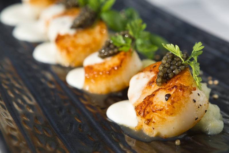 A dark plate with scallop entrees and greenery