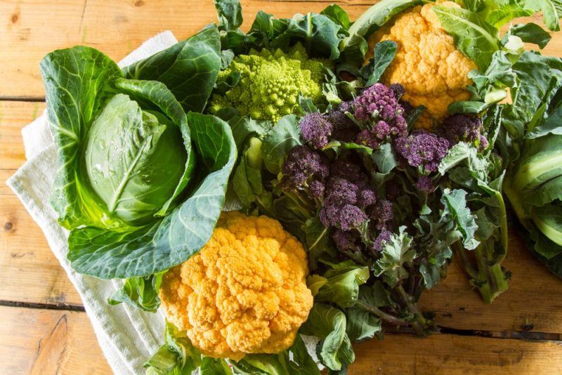 A selection of green, yellow and purple cruciferous vegetables on a wooden table