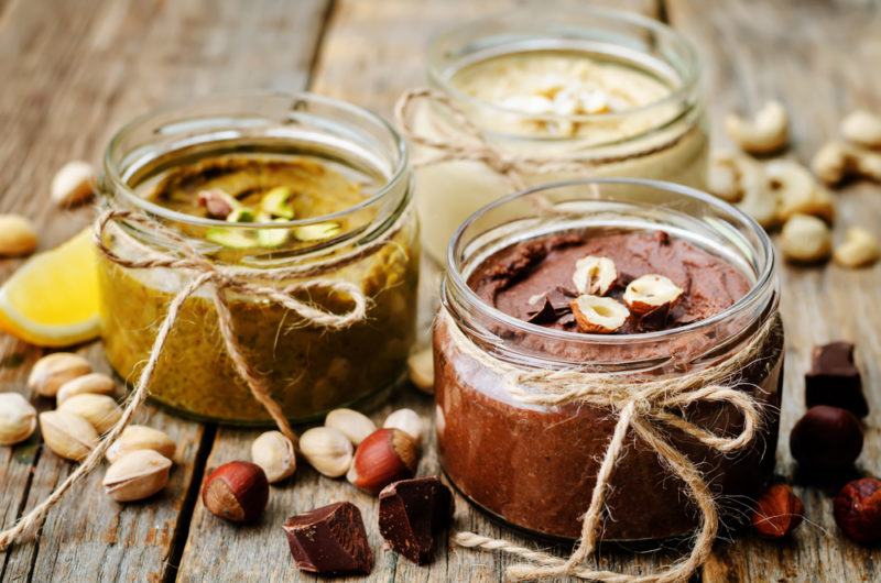 Three types of nut butter with nuts on a table