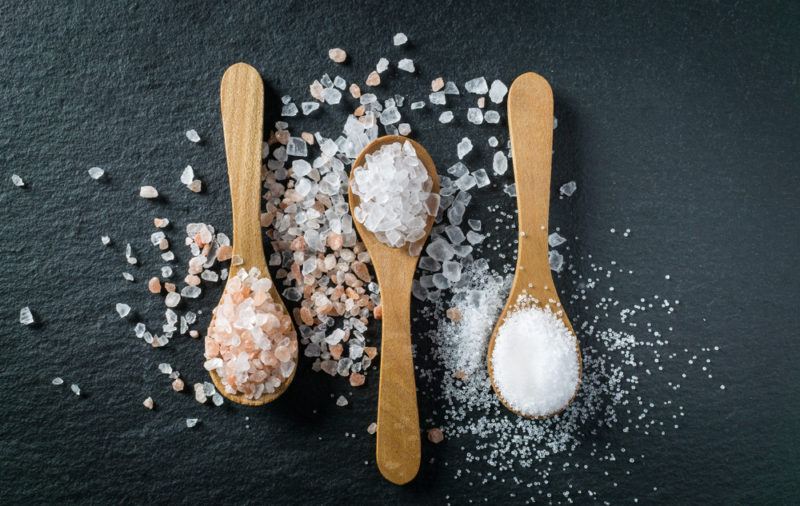 Three wooden spoons with various types of salt on a black background